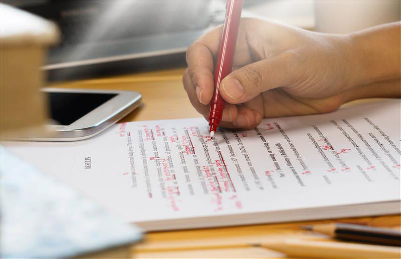 person editing a paper with red pen