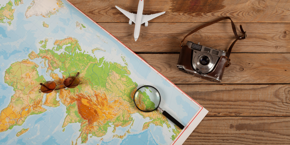 A map with a magnifying glass on a table with a camera and toy airplane