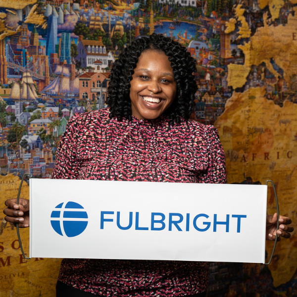 Abaneh Ebangwese holds a Fulbright banner in front of a large map