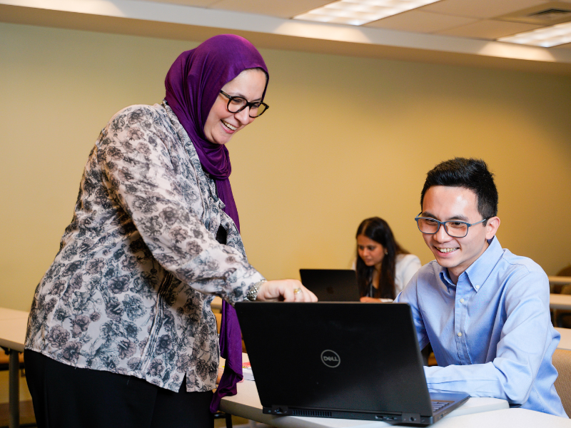 Dr. Danya Qato works with a student on a laptop