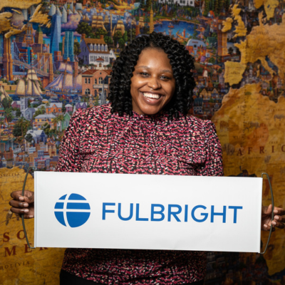 Abaneh Ebangwese poses with a Fulbright banner in front of a large map