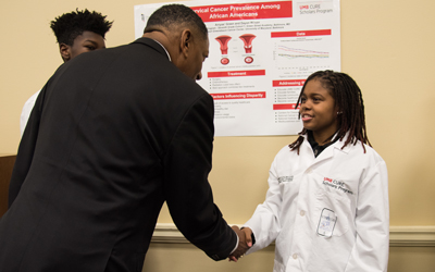 Baltimore City Del. Keith Haynes (left) shakes hands with Aniyaa Green (right), a cohort one scholar, before she presents her research poster. 